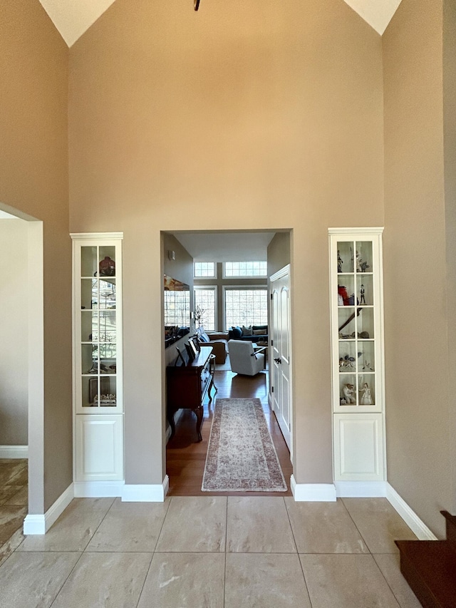 interior space featuring baseboards, high vaulted ceiling, and light tile patterned flooring