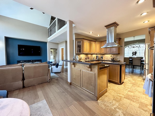 kitchen featuring island range hood, a peninsula, a kitchen breakfast bar, decorative backsplash, and dark countertops