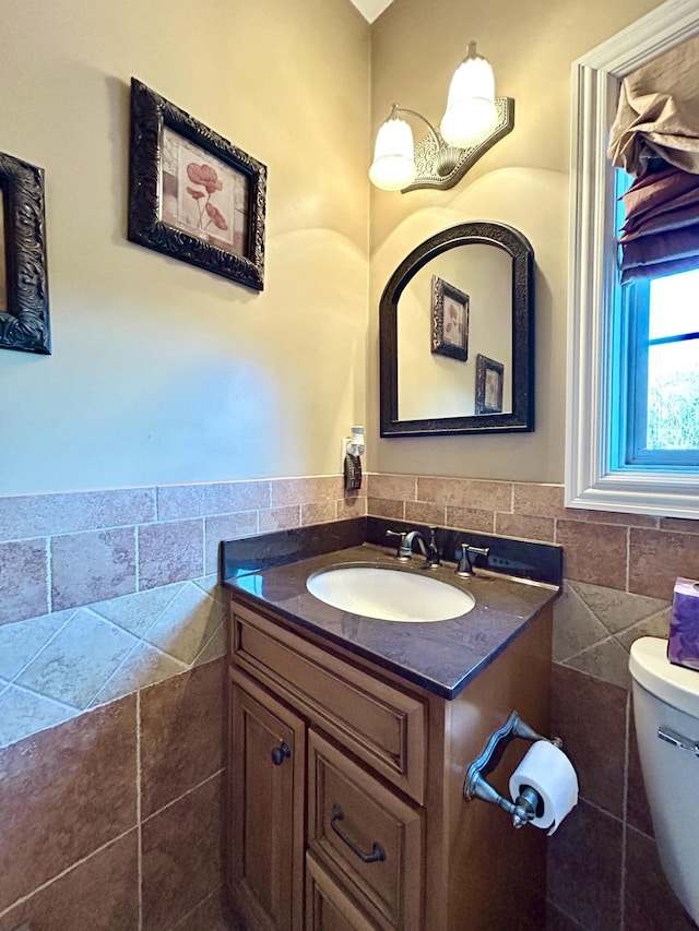 bathroom with toilet, a wainscoted wall, tile walls, and vanity