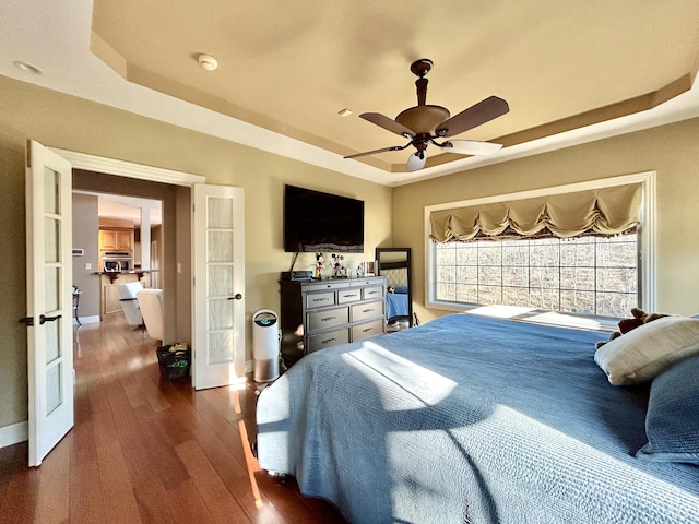 bedroom with dark wood-style floors, french doors, a raised ceiling, a ceiling fan, and baseboards