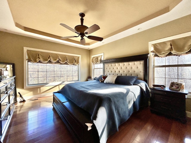 bedroom with dark wood-style floors, visible vents, a tray ceiling, and a ceiling fan