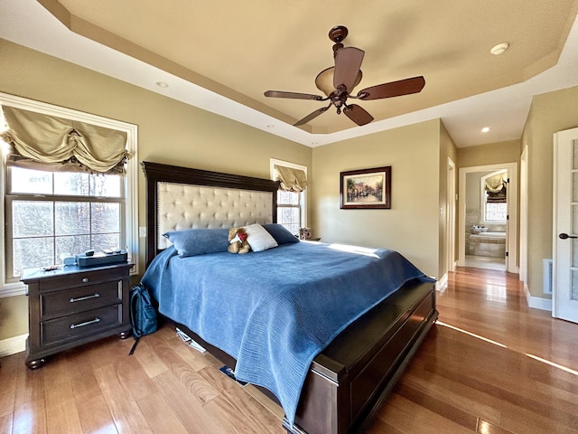 bedroom with a tray ceiling, multiple windows, wood finished floors, and baseboards