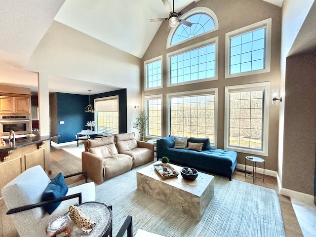 living room featuring high vaulted ceiling, ceiling fan, and baseboards