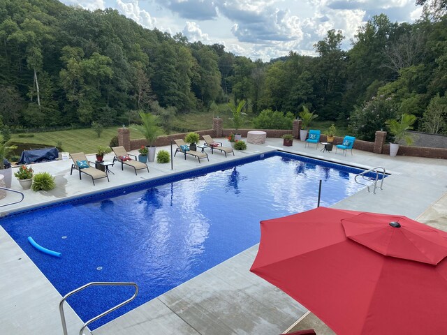 outdoor pool with a patio and a wooded view