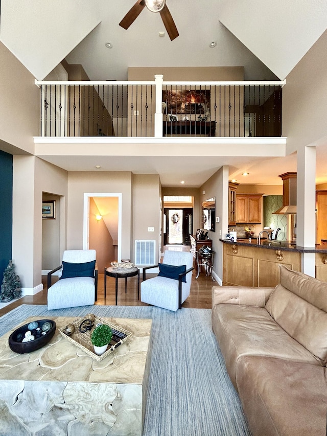 living area featuring light wood-style floors, ceiling fan, baseboards, and high vaulted ceiling