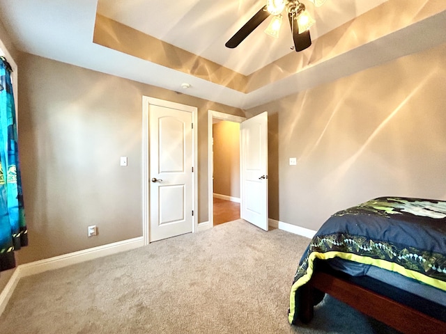 carpeted bedroom with baseboards, a raised ceiling, and a ceiling fan