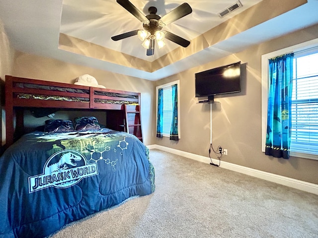 carpeted bedroom featuring a ceiling fan, a raised ceiling, visible vents, and baseboards