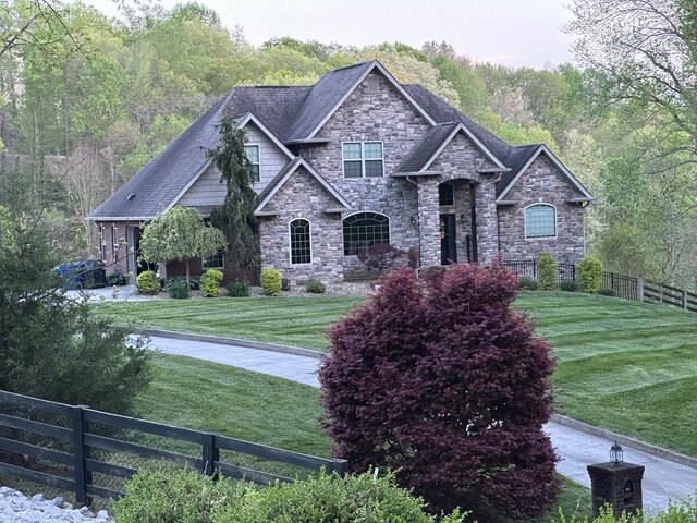 view of front facade featuring a shingled roof, fence, and a front lawn