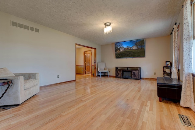 living room with a textured ceiling, a fireplace, wood finished floors, and visible vents