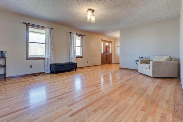 unfurnished living room with light wood-type flooring, visible vents, a textured ceiling, and baseboards