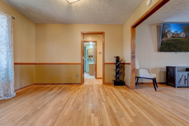 spare room featuring a textured ceiling, baseboards, and wood finished floors