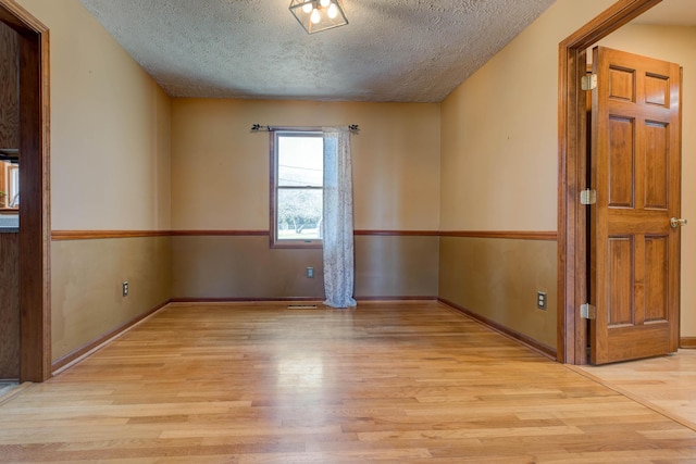 spare room featuring baseboards, light wood-style flooring, and a textured ceiling