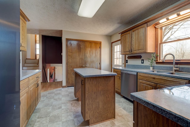 kitchen featuring dishwasher, a kitchen island, a textured ceiling, light floors, and a sink