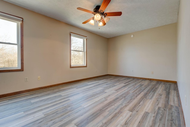 empty room with light wood-style floors, a ceiling fan, baseboards, and a textured ceiling