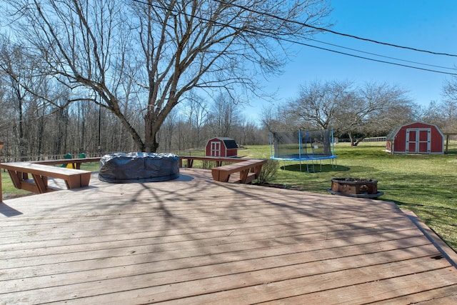 deck with a storage shed, an outdoor fire pit, a lawn, an outbuilding, and a trampoline