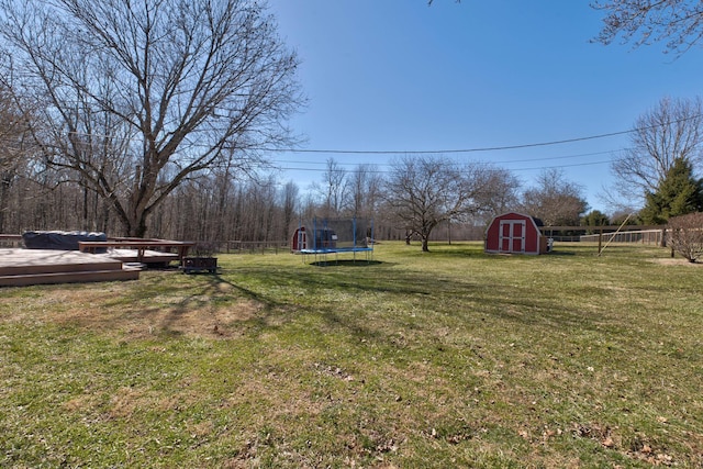 view of yard featuring a trampoline, an outdoor structure, fence, and a storage unit