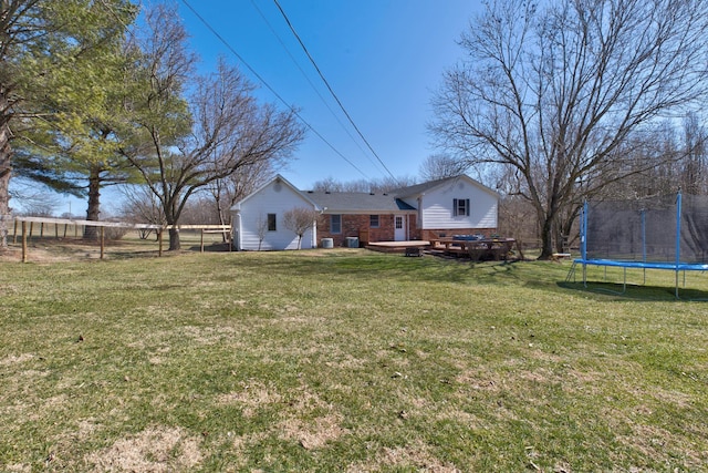 view of yard featuring a deck, a trampoline, and fence