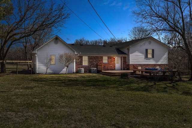 back of house at dusk with fence, a deck, a yard, central air condition unit, and brick siding