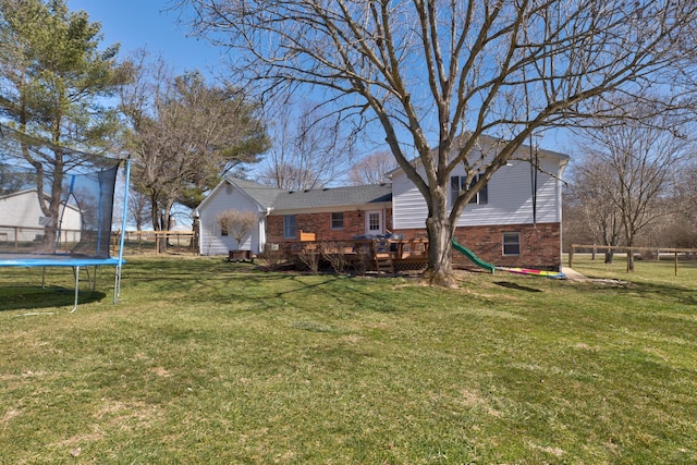 view of yard featuring a deck, a trampoline, and fence