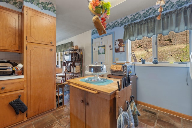 kitchen featuring stone tile floors, visible vents, wooden counters, backsplash, and baseboards