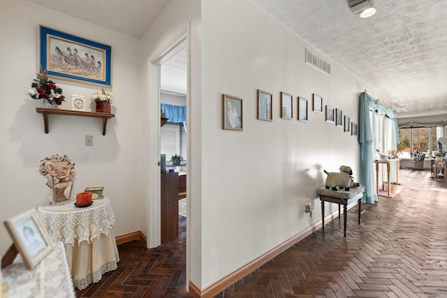 hall featuring visible vents, a textured ceiling, and baseboards