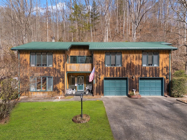 view of front of property featuring an attached garage, metal roof, driveway, and a front lawn