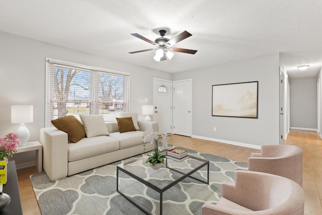 living area featuring light wood finished floors, ceiling fan, baseboards, and a textured ceiling