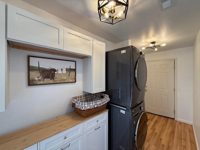 laundry area with visible vents, light wood-style flooring, cabinet space, an inviting chandelier, and stacked washer / drying machine