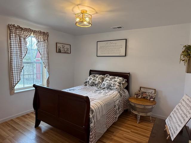 bedroom with wood finished floors, visible vents, and baseboards