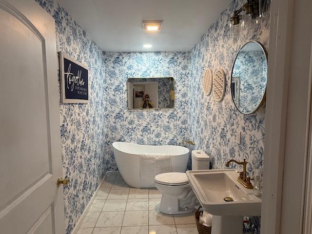 full bath featuring a soaking tub, toilet, wallpapered walls, and a sink