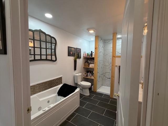 bathroom featuring a shower stall, a jetted tub, and toilet