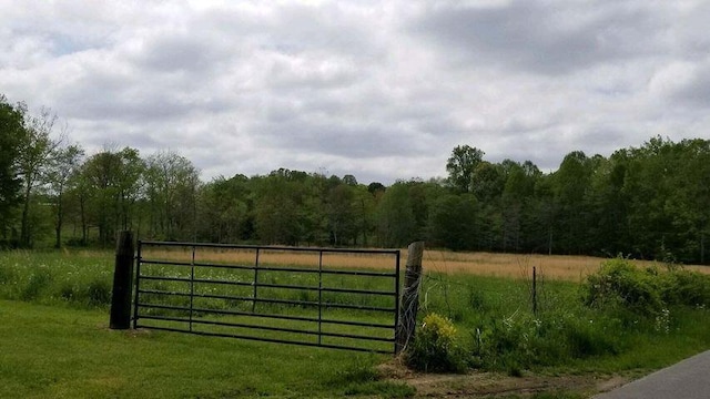 view of gate featuring a rural view, a wooded view, and a lawn