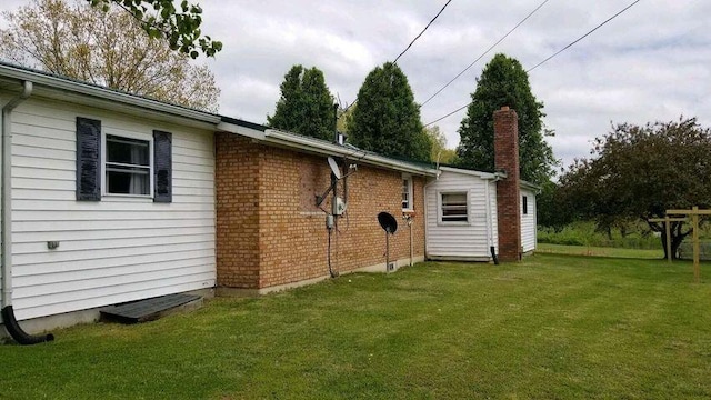 exterior space featuring brick siding, a lawn, and a chimney