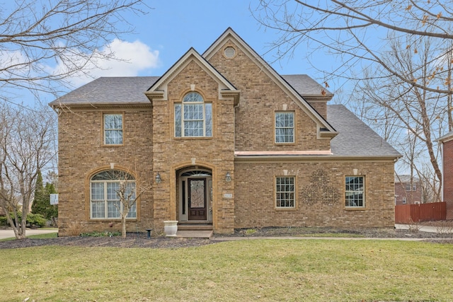 traditional-style house featuring a shingled roof, a front lawn, and brick siding