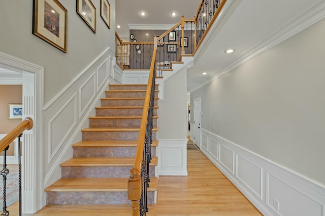 staircase with crown molding, a decorative wall, and wood finished floors