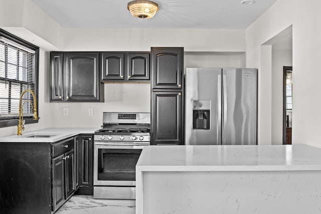 kitchen featuring marble finish floor, appliances with stainless steel finishes, a sink, and dark cabinetry