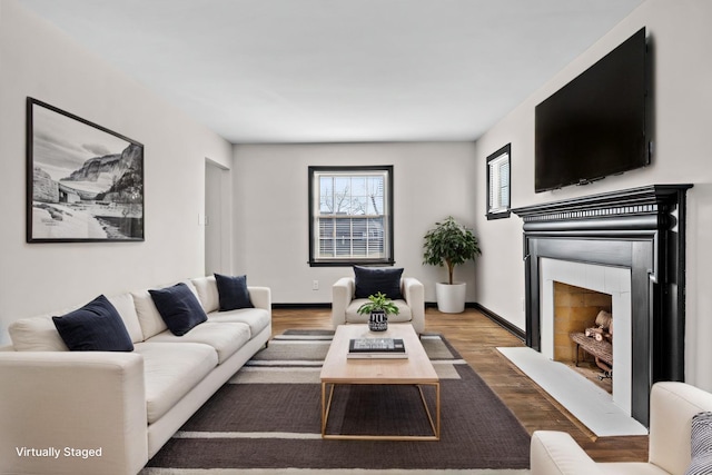 living room featuring a fireplace with flush hearth, baseboards, and wood finished floors