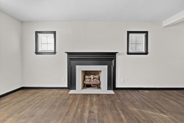 unfurnished living room with wood finished floors, a fireplace with flush hearth, visible vents, and baseboards