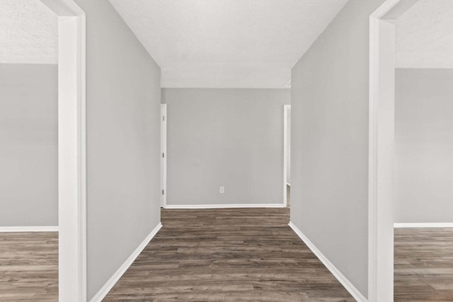 corridor featuring a textured ceiling, baseboards, and wood finished floors