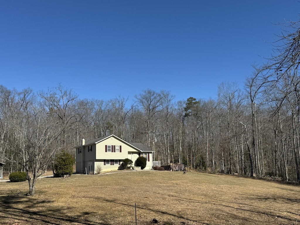 exterior space with a chimney, a view of trees, and a yard