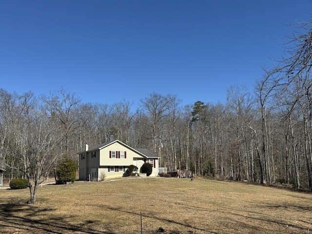 exterior space with a chimney, a view of trees, and a yard