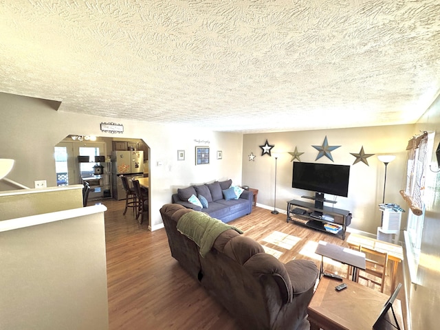 living area with baseboards, a textured ceiling, arched walkways, and wood finished floors