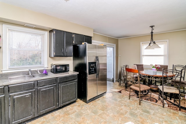 kitchen featuring pendant lighting, light countertops, a sink, dark cabinetry, and stainless steel fridge with ice dispenser