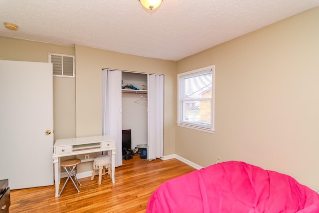 bedroom featuring a closet, visible vents, a textured ceiling, wood finished floors, and baseboards