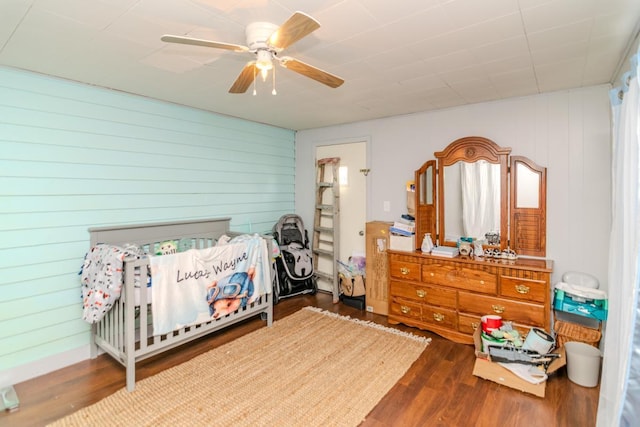 bedroom with ceiling fan, wooden walls, and wood finished floors