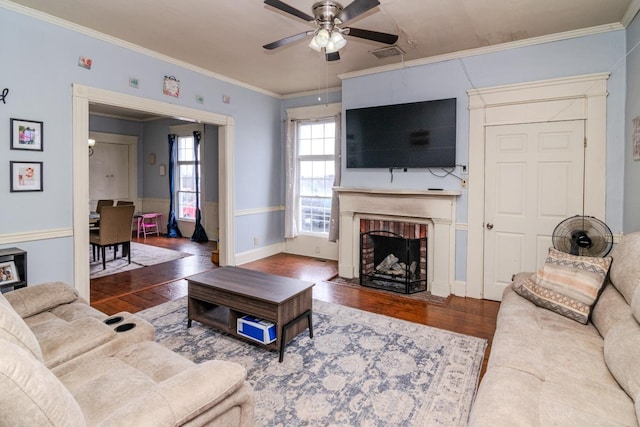 living room with a ceiling fan, a brick fireplace, crown molding, and wood finished floors