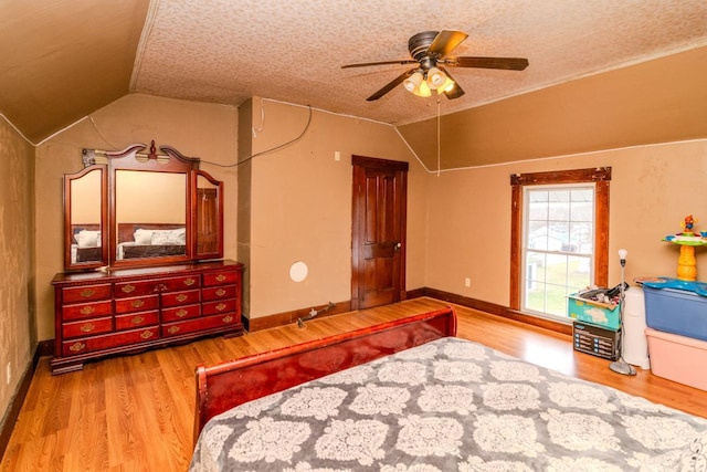 bedroom with a ceiling fan, vaulted ceiling, a textured ceiling, wood finished floors, and baseboards