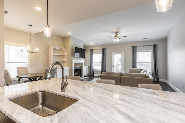 kitchen featuring plenty of natural light, visible vents, light stone counters, a fireplace, and a sink