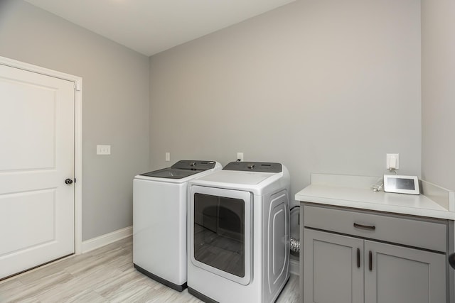 clothes washing area with light wood-style flooring, independent washer and dryer, cabinet space, and baseboards