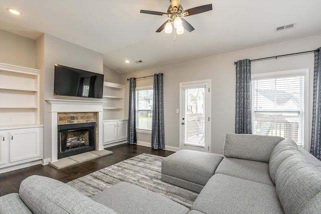 living area featuring baseboards, visible vents, dark wood-type flooring, vaulted ceiling, and a stone fireplace